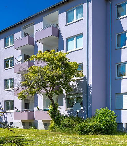 Das Foto zeigt ein Mehrfamilienhaus in Hattersheim. Dieses liegt an einer Grünfläche mit einem beschattenden Baum.
