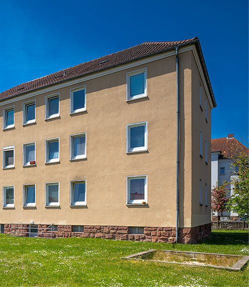 Das Foto eines Mehrfamilienhauses in Fulda. Das Haus liegt an einer Grünfläche mit einem Sandkasten.